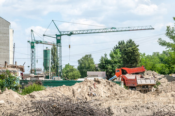 Ground excavation site with heavy tipper trucks and construction cranes on the new residential building terrain preparation, with blue sky background