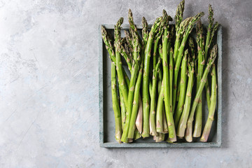 Raw uncooked organic green asparagus in wooden tray over grey texture background. Top view, copy space.