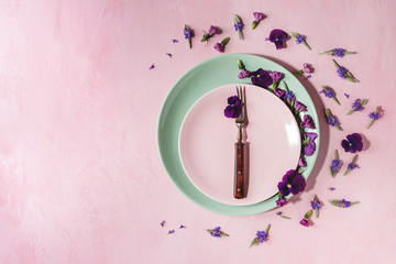 Variety of purple edible flowers for dish decorating with empty ceramic plate and fork over pink pastel background. Top view, space. - Powered by Adobe