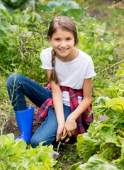Beautiful smiling girl spudding earth with small trowel in garden