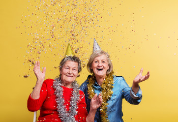 Portrait of a senior women in studio on a yellow background. Party concept.