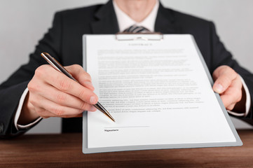 Businessman indicates the place for signing in the contract,which is attached to a clipboard.