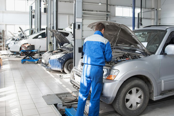 A mechanic working in a car workshop in a blue working form is repairing a gray car. Auto service.