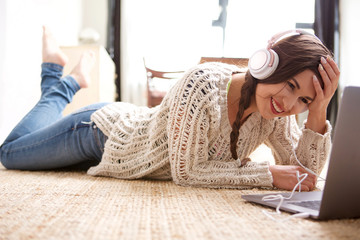 Obraz premium attractive young woman lying on floor at home with laptop and headphones