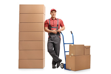 Mover with a hand truck leaning on a stack of boxes and smiling