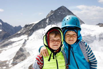 Fototapeta na wymiar Two little boys with safety helmets and clothing with mountains landscape backgrounds. Kids hiking and discovering glacier in Tirol, Austria, Hintertux