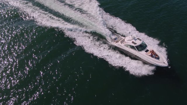 Drone shot of yacht sailing in the ocean waters with people sitting in front deck. Group of men and women relaxing on private yacht deck.
