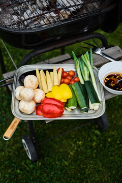Overhead view of tray of colorful raw vegetables on side of barbecue waiting to be grilled