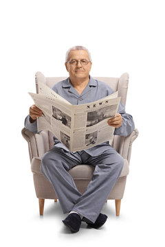 Mature man seated in an armchair holding a newspaper and looking at the camera