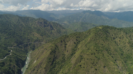 Aerial view of mountain river in the cordillera, road on the slopes, mountains covered forest, trees. Cordillera region. Luzon, Philippines. Mountain landscape sky with clouds.