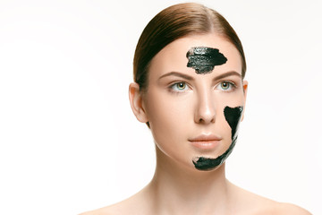 Young beautiful woman applying a mask for the face of the therapeutic black mud. Spa treatment