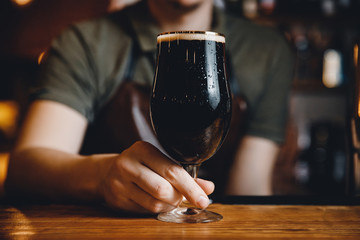 Barman serves glass of dark cold beer at bar counter.