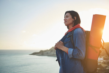 Profile of young lady with backpack and yoga mat looking at calm water of sea. Copy space in left side