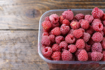 fresh raspberries in a plastic container on a wooden background