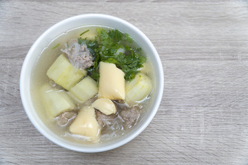 close-up shot top view of a white bowl of Clear soup vermicelli with Stir-fried pork chops, stuffed with cucumber on wooden table background in the daytime.