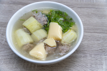 close-up shot top view of a white bowl of Clear soup vermicelli with Stir-fried pork chops, stuffed with cucumber on wooden table background in the daytime.