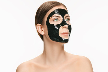 Young beautiful woman applying a mask for the face of the therapeutic black mud. Spa treatment