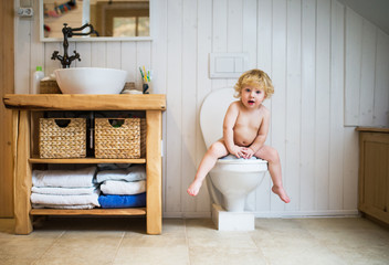Cute toddler boy sitting on the toilet in the bathroom.