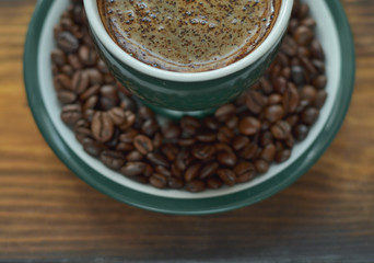 A cup of hot coffee with foam on a saucer with coffee beans