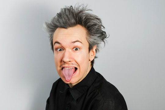 Young guy shows tongue like Albert Einstein on gray background.