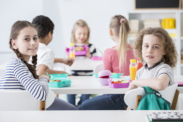 Smiling girl and boy eating healthy breakfast during break at school