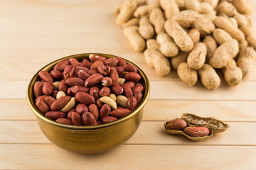 Bronze bowl of peeled peanuts and peanuts in nutshell on wooden table
