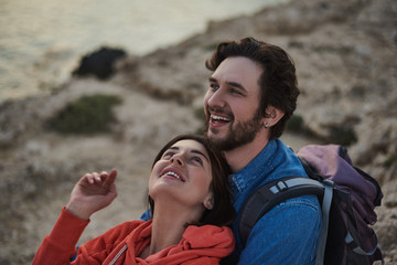 Happy together. Portrait of excited young man enjoying the nature while embracing his wife. Woman is looking at husband with love