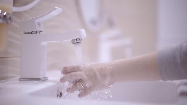 Two unrecognizable little girls with long fair hair washing their hands in a bathroom. Concept of hygiene and family time. Left to right pan real time close up shot