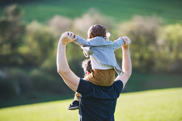 A father giving toddler son piggyback ride outside in spring nature.