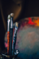 Naklejka premium Paintbrushes in the glass in a vertical position closeup. A colorful palette with oil paints on the background