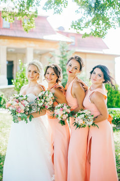 Stylish Young Smiling Blonde Bride With Her Bridesmaids In Peach Summer Dress In The Park On Her Happy Wedding Day. Women In The Same Color Dress. All Brunette One Blonde.