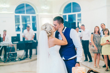 Naklejka premium Newlyweds cutting their delicious wedding cake. Wedding restaurant reception hall. Bride and groom stay near they wedding cake in peach color.