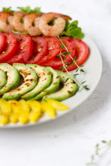 Avocado salad on a white background. Avocado, tomato, pepper and shrimps on a plate lined with rows