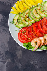 Avocado, tomato, pepper and shrimps on a plate lined with rows. Avocado salad on a dark background