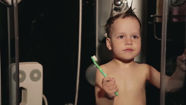 Little funny boy 2-3 years old brush his teeth in the shower and laughs. The child is going to sleep