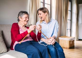 Elderly grandmother and adult granddaughter at home, knitting.