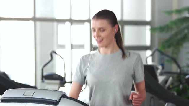 Young slim woman exercising at gym. Pretty girl runs on machine at modern fitness club. Be in shape.