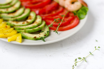 Avocado salad on a white background. Avocado, tomato, pepper and shrimps on a plate lined with rows