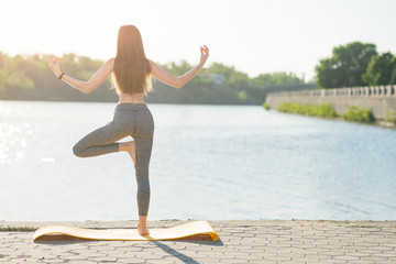 A young girl is engaged in yoga on the waterfront at dawn or sunset. The concept of vivacity, a healthy lifestyle, spirituality of the body, energy and interaction with nature
