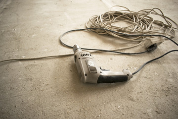 the old electric drill rests on the concrete floor, near the extension cord with a socket