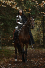 A beautiful warrior girl with a sword wearing chainmail and armor riding a horse in a mysterious forest. © artyme