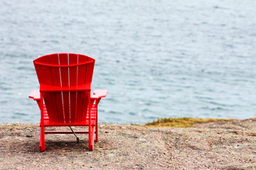 A red Adirondack chair anchored to the cliff, facing out toward the sea, trail side, Signal Hill, St. John's, Newfoundland Labrador.