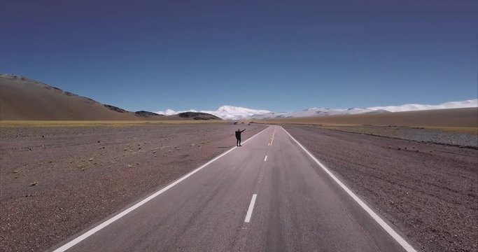 Lonely hitchhiker  with backpack walking along highway road in the beautiful andean mountains of Argentina. Concept of travel, wanderlust and adventure, aerial view. 4k