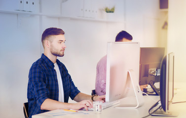 business, technology, education and people concept - young creative man or student with computer at office