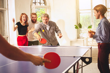 Group of happy young friends playing ping pong table tennis