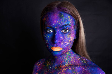 Creative make-up and beauty theme: beautiful girl model with cosmic make-up on face and body blue and purple skin color on dark background in studio