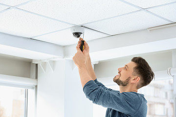 Technician installing CCTV camera on ceiling indoors
