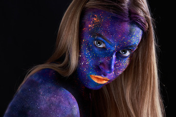 Creative make-up and beauty theme: beautiful girl model with cosmic make-up on face and body blue and purple skin color on dark background in studio