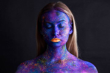 Young artistic woman in black paint and colourful powder. Glowing dark makeup. Creative body art on the theme of space and stars. Bodypainting project: art, beauty, fashion.