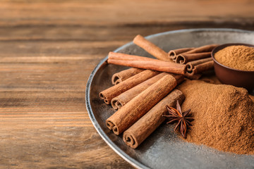 Plate with aromatic cinnamon powder and sticks on wooden table